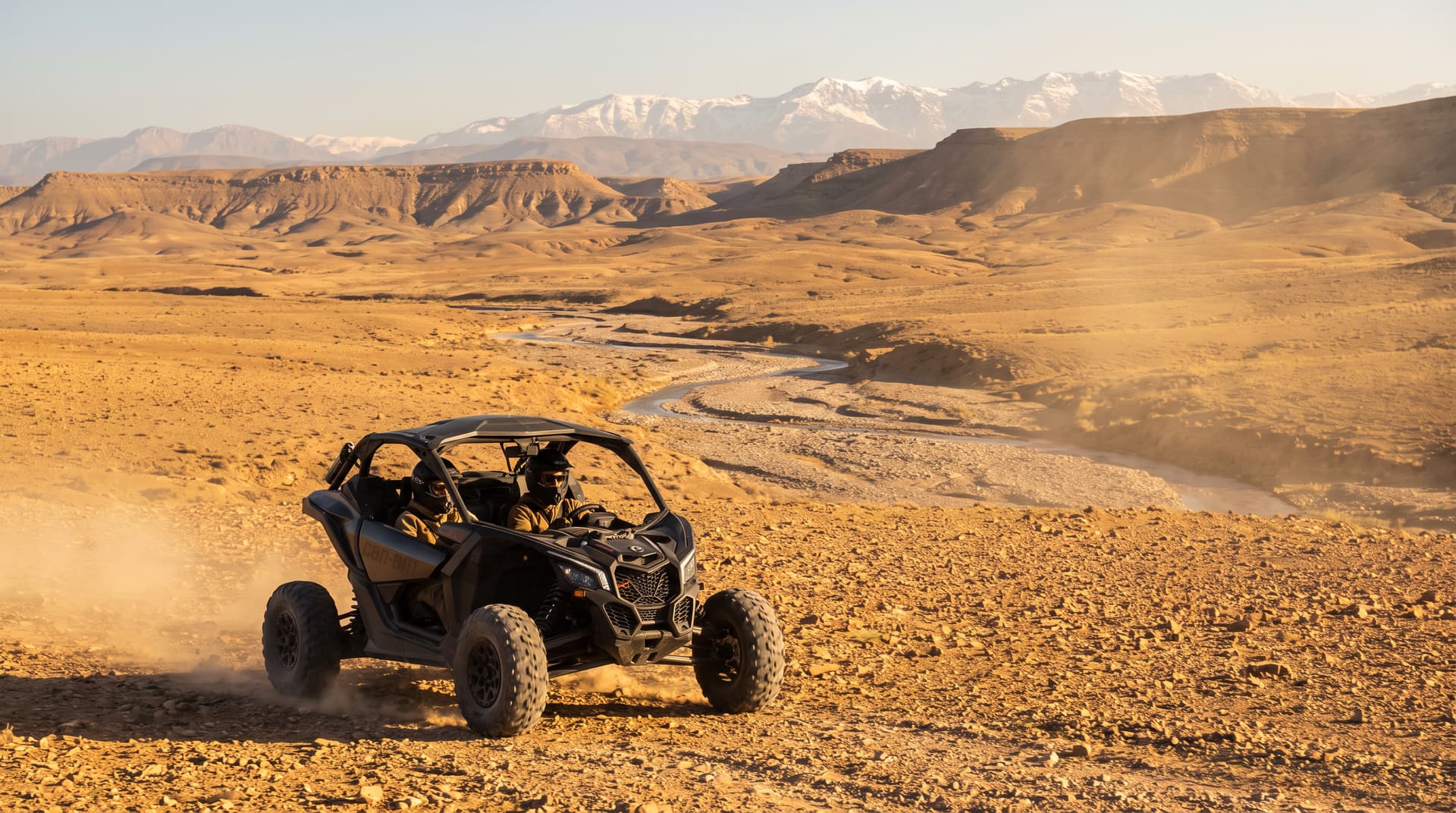 Buggy Can-Am Maverick X3 sur un plateau rocheux du désert d'Agafay, oued asséché et chaîne de l'Atlas enneigée à l'horizon